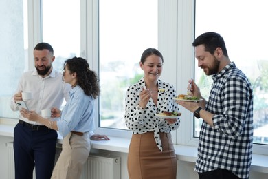 Photo of Colleagues with food and drinks near window in office during lunch break
