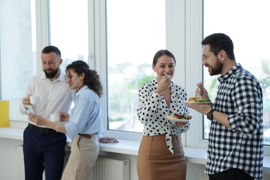 Photo of Colleagues with food and drinks near window in office during lunch break
