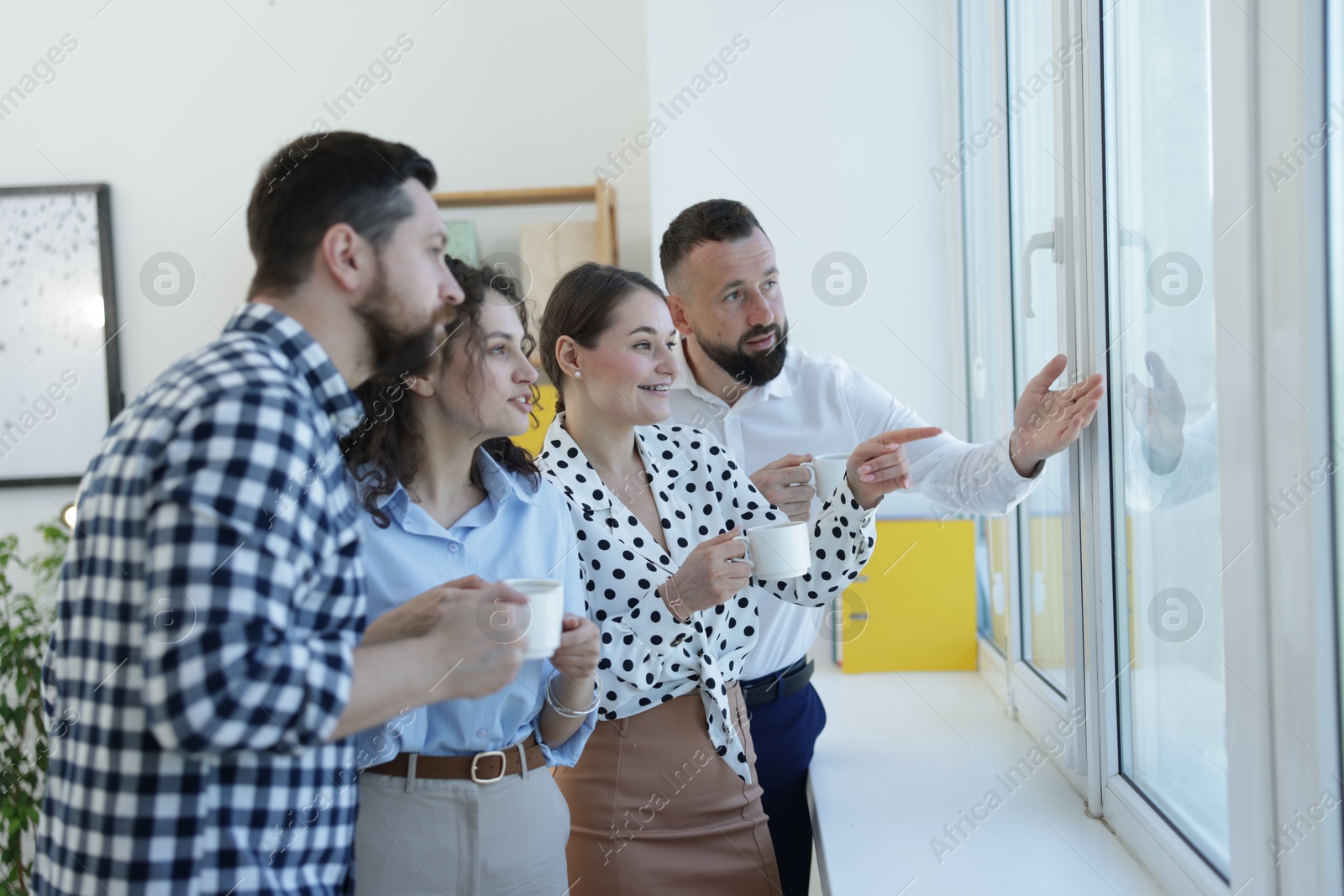Colleagues looking out window during coffee break in office Photo of Colleagues looking out window during coffee break in office