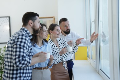 Photo of Colleagues looking out window during coffee break in office