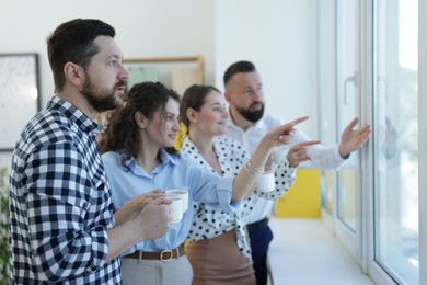 Photo of Colleagues looking out window during coffee break in office
