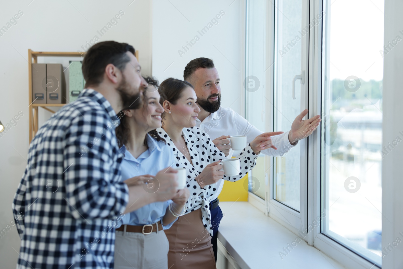 Colleagues looking out window during coffee break in office Photo of Colleagues looking out window during coffee break in office