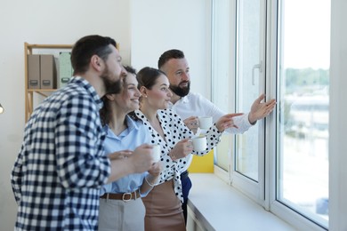 Photo of Colleagues looking out window during coffee break in office
