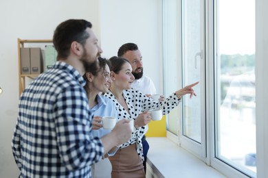 Photo of Colleagues looking out window during coffee break in office