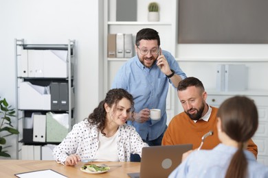 Photo of Colleagues eating and chatting during lunch break in office