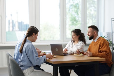Photo of Colleagues eating and chatting during lunch break in office