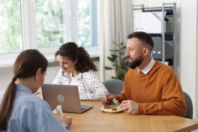 Photo of Colleagues eating and chatting during lunch break in office