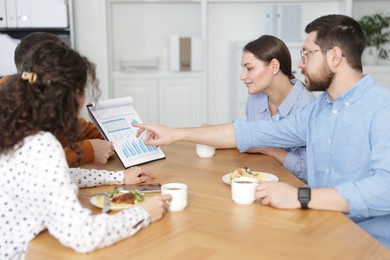 Photo of Colleagues eating and discussing work during lunch break in office
