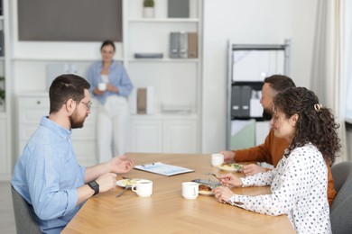 Photo of Colleagues eating and chatting during lunch break in office