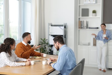 Photo of Colleagues eating and chatting during lunch break in office