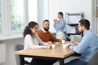 Photo of Colleagues eating and chatting during lunch break in office