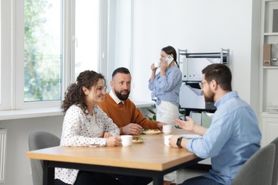 Photo of Colleagues eating and chatting during lunch break in office