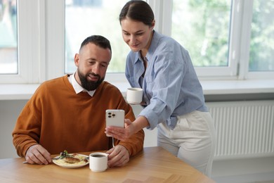 Photo of Woman showing her colleague something on smartphone during lunch break in office