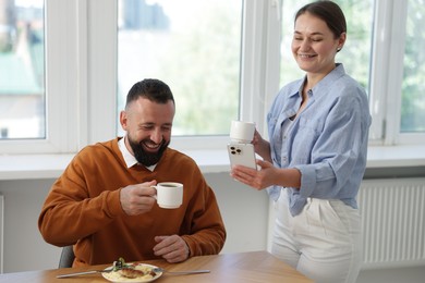 Photo of Woman showing her colleague something on smartphone during lunch break in office
