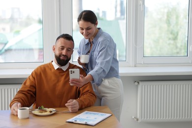 Photo of Woman showing her colleague something on smartphone during lunch break in office