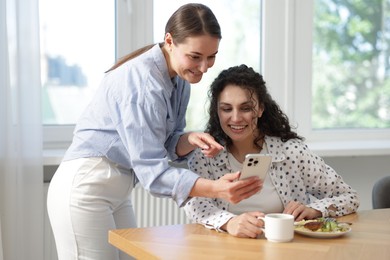 Photo of Woman showing her colleague something on smartphone during lunch break in office