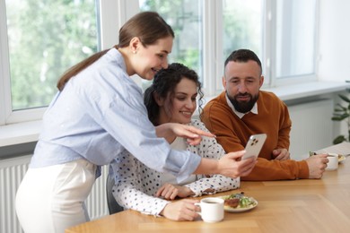 Photo of Woman showing her colleagues something on smartphone during lunch break in office