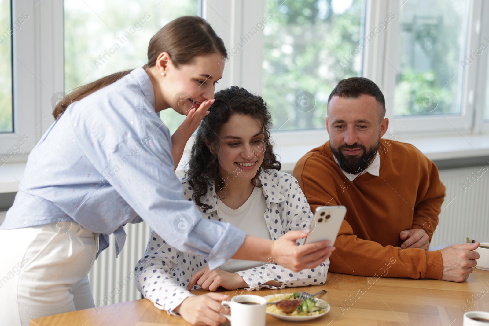 Woman showing her colleagues something on smartphone during lunch break in office Photo of Woman showing her colleagues something on smartphone during lunch break in office