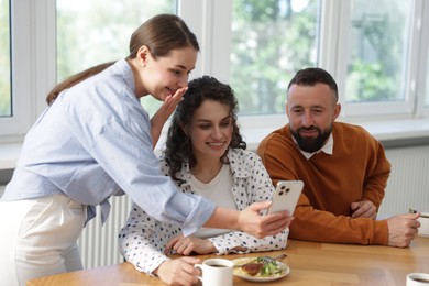 Photo of Woman showing her colleagues something on smartphone during lunch break in office
