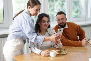 Photo of Woman showing her colleagues something on smartphone during lunch break in office