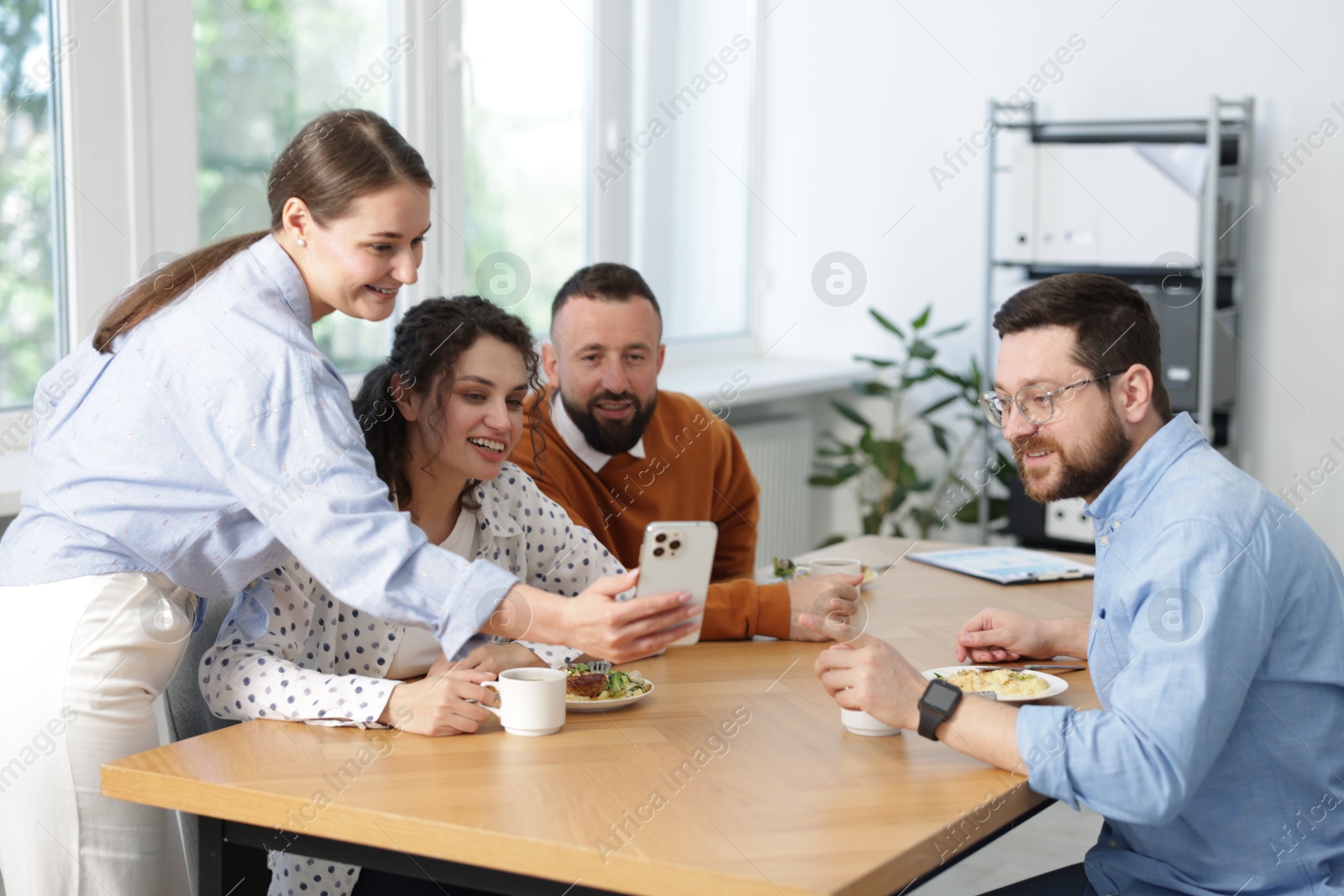Woman showing her colleagues something on smartphone during lunch break in office Photo of Woman showing her colleagues something on smartphone during lunch break in office