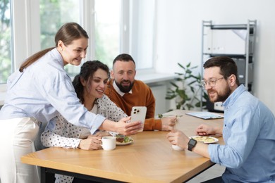 Photo of Woman showing her colleagues something on smartphone during lunch break in office
