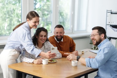 Photo of Woman showing her colleagues something on smartphone during lunch break in office