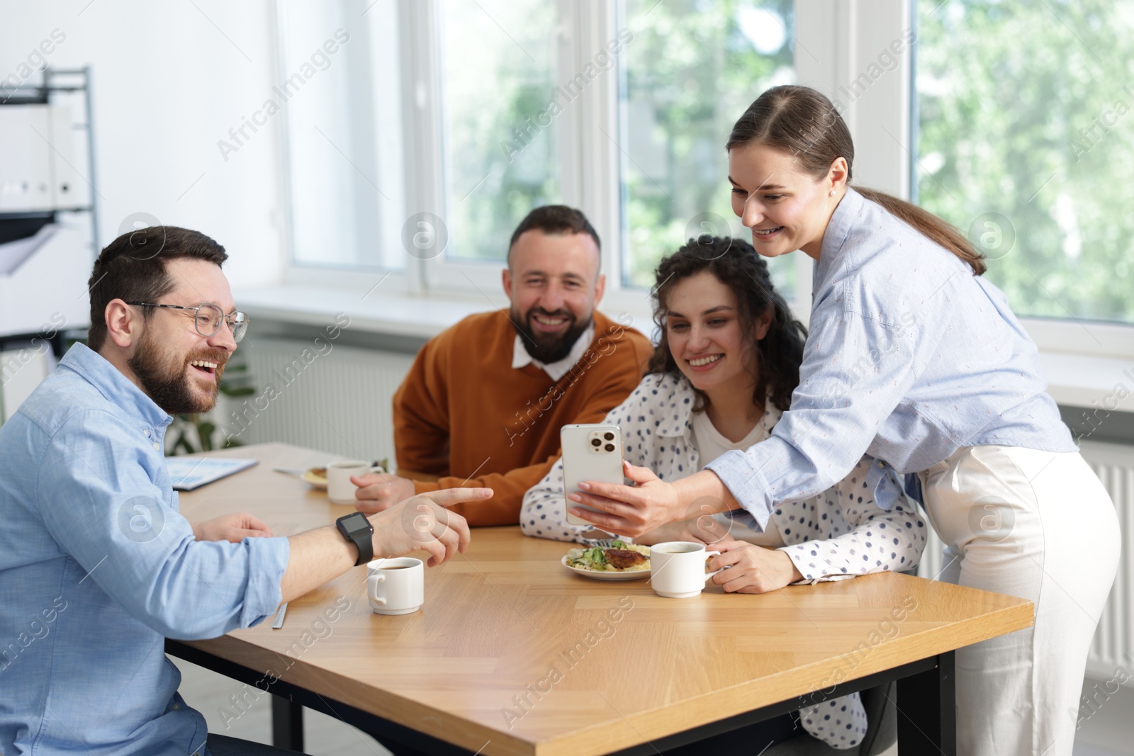 Woman showing her colleagues something on smartphone during lunch break in office Photo of Woman showing her colleagues something on smartphone during lunch break in office