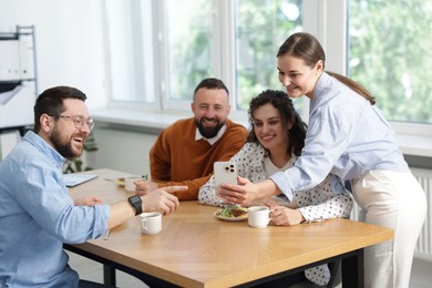 Photo of Woman showing her colleagues something on smartphone during lunch break in office