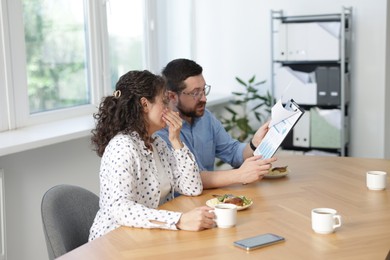 Photo of Colleagues eating and discussing work during lunch break in office