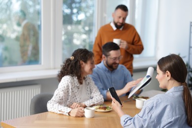 Photo of Colleagues eating and discussing work during lunch break in office