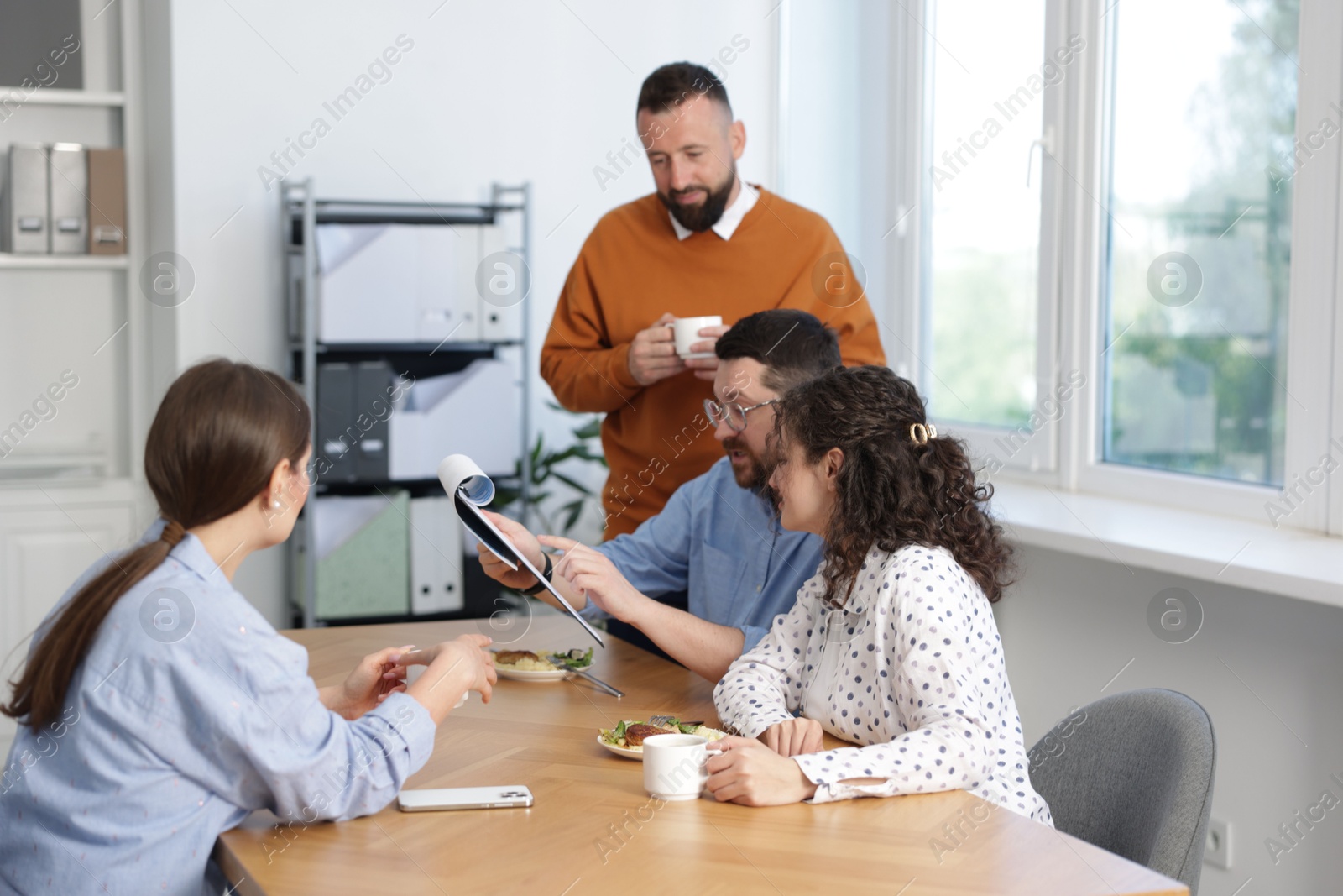 Colleagues eating and discussing work during lunch break in office Photo of Colleagues eating and discussing work during lunch break in office