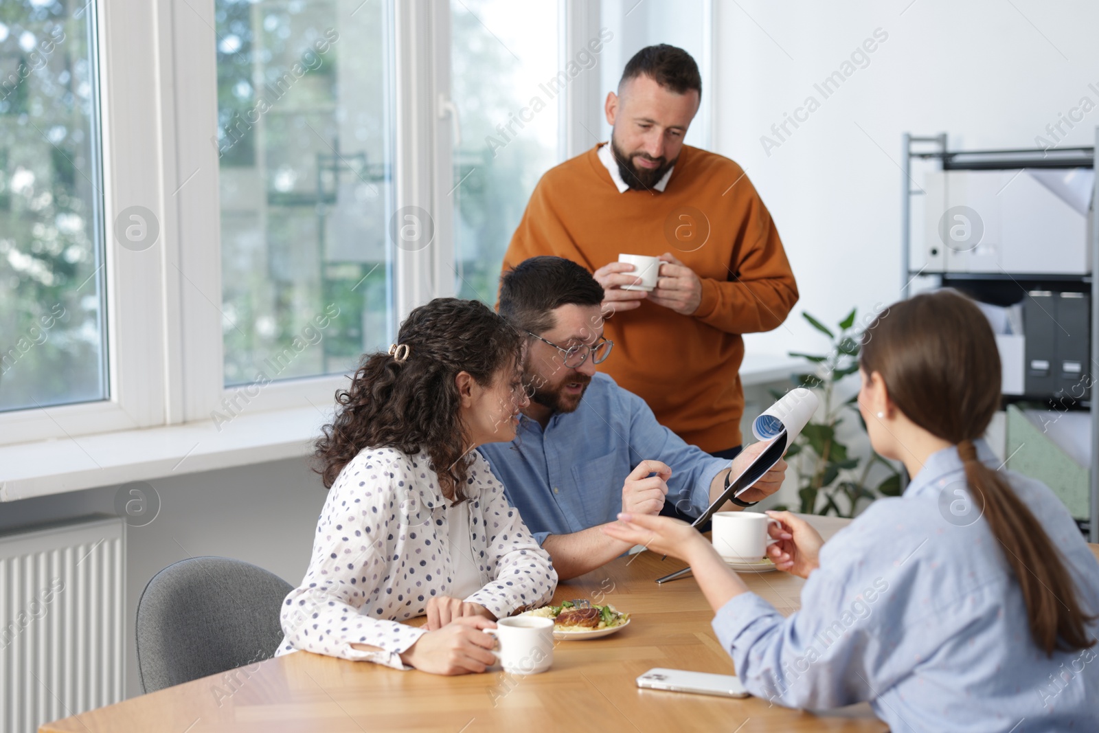 Colleagues eating and discussing work during lunch break in office Photo of Colleagues eating and discussing work during lunch break in office
