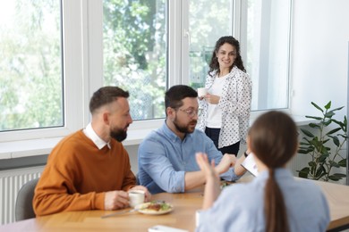 Photo of Colleagues eating and discussing work during lunch break in office
