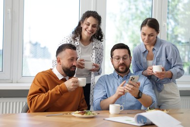 Photo of Man showing his colleagues something on smartphone during lunch break in office