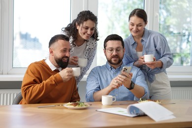 Photo of Man showing his colleagues something on smartphone during lunch break in office