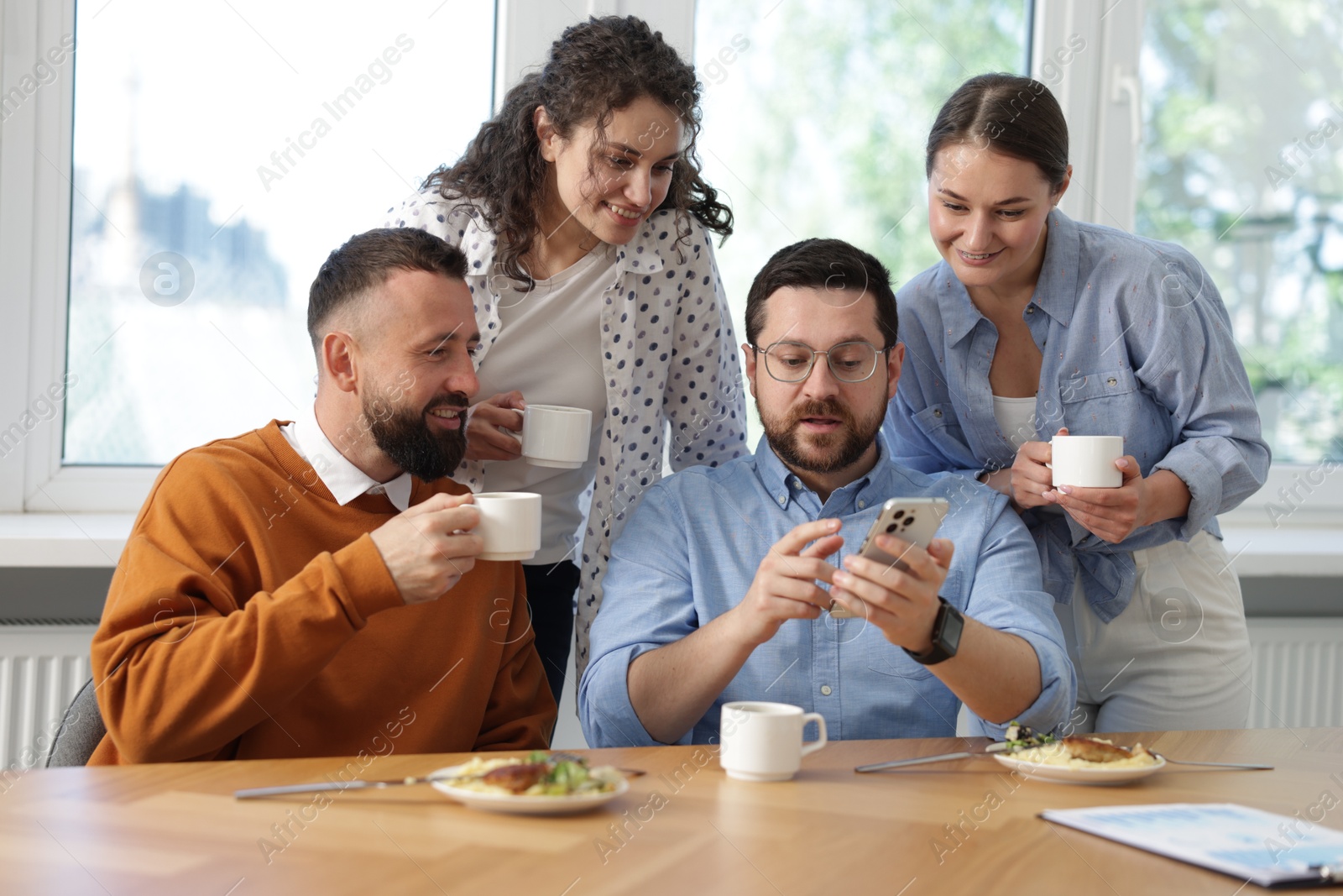 Man showing his colleagues something on smartphone during lunch break in office Photo of Man showing his colleagues something on smartphone during lunch break in office