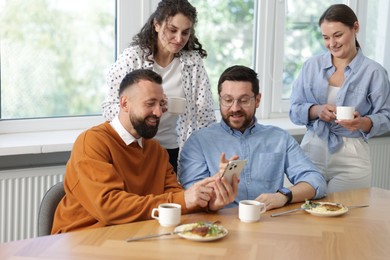 Photo of Man showing his colleagues something on smartphone during lunch break in office