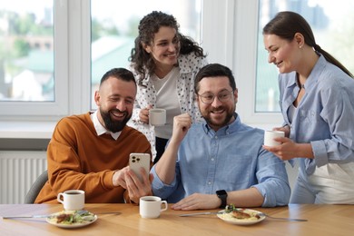 Photo of Man showing his colleagues something on smartphone during lunch break in office