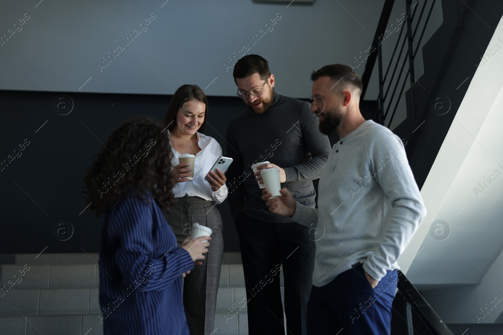 Colleagues with coffee on stairs in office during break Photo of Colleagues with coffee on stairs in office during break