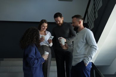 Photo of Colleagues with coffee on stairs in office during break