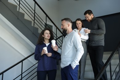 Photo of Colleagues with coffee on stairs in office during break