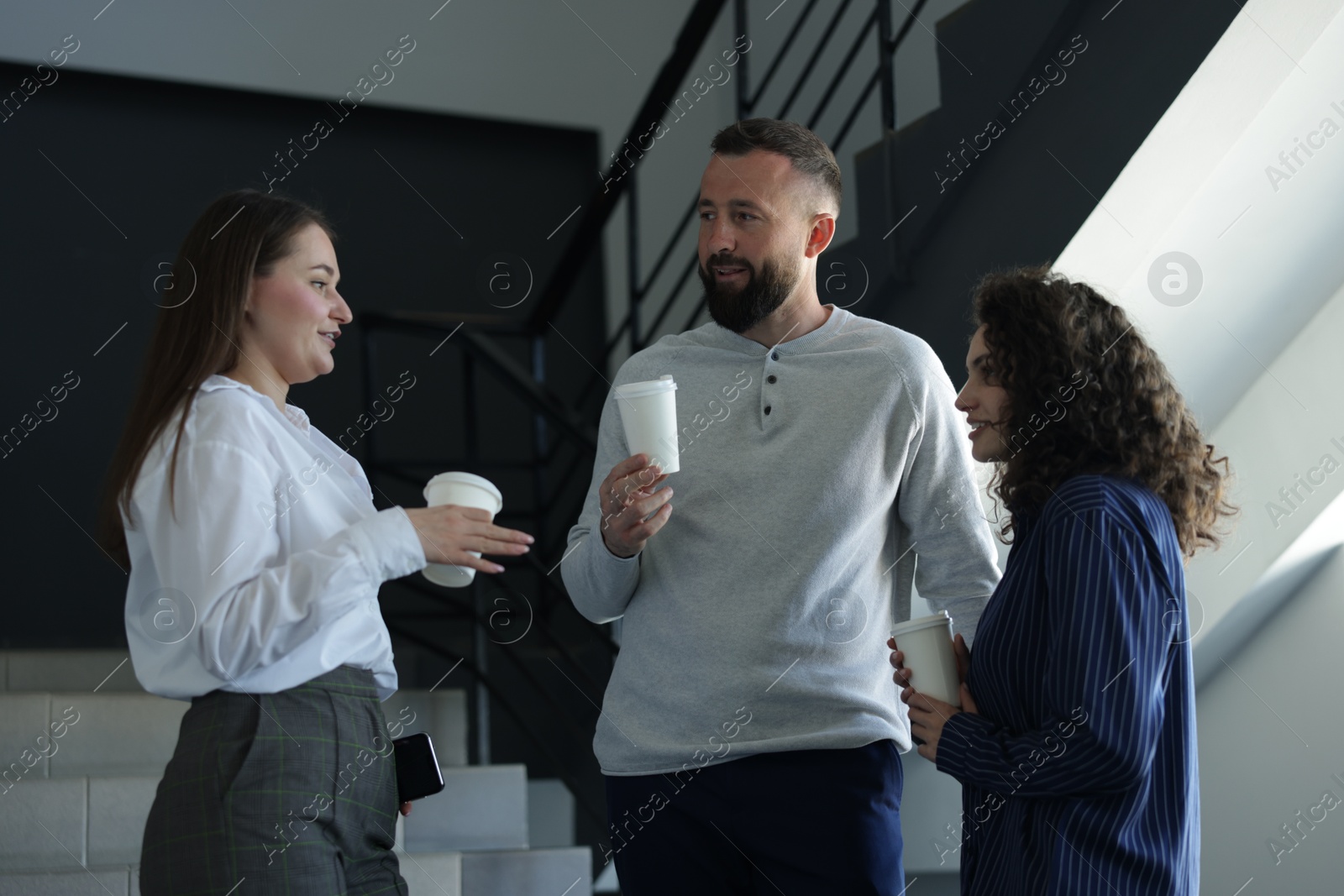 Colleagues with coffee on stairs in office during break Photo of Colleagues with coffee on stairs in office during break