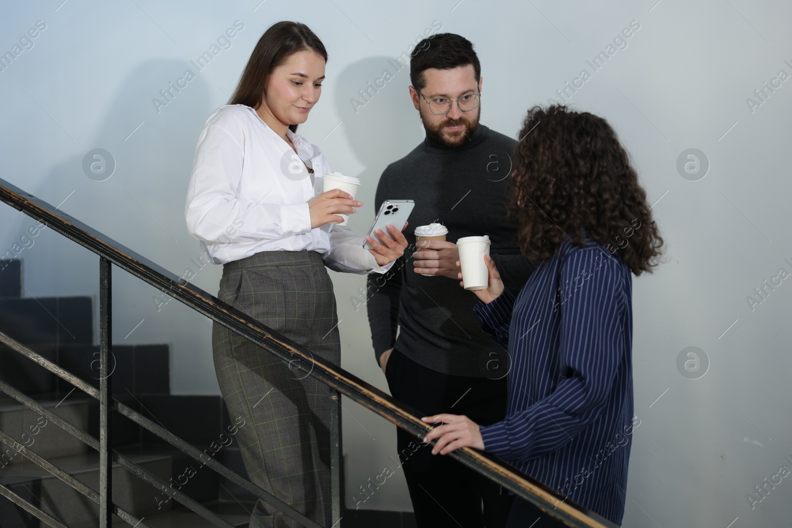 Colleagues with coffee on stairs in office during break Photo of Colleagues with coffee on stairs in office during break