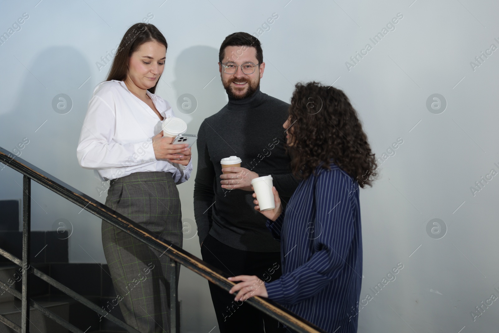 Colleagues with coffee on stairs in office during break Photo of Colleagues with coffee on stairs in office during break
