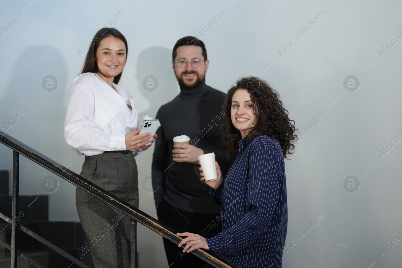 Colleagues with coffee on stairs in office during break Photo of Colleagues with coffee on stairs in office during break