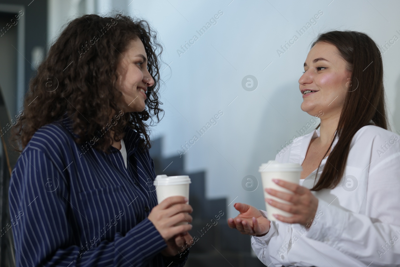 Colleagues with coffee on stairs in office during break Photo of Colleagues with coffee on stairs in office during break