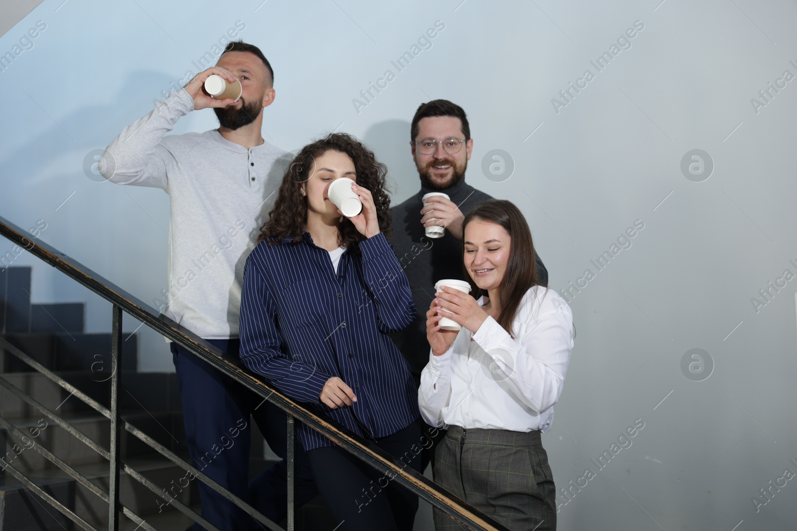 Colleagues with coffee on stairs in office during break Photo of Colleagues with coffee on stairs in office during break