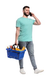 Photo of Man with shopping basket full of products talking on smartphone against white background