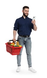 Photo of Man with shopping basket full of products and smartphone on white background